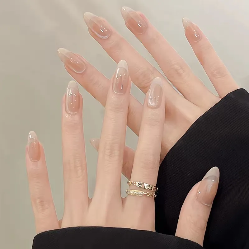 Close-up of a hand with clear nail polish and a gold ring on a neutral background