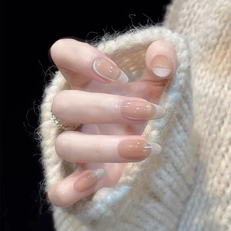 Close-up of a hand with beige nail polish wearing a white knitted sweater.