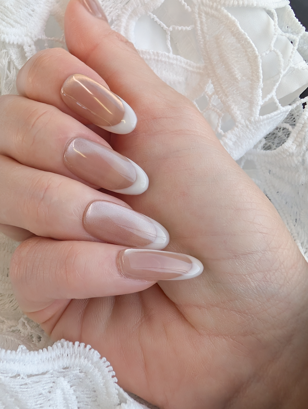Hand with nude-colored nail polish on a white lace background