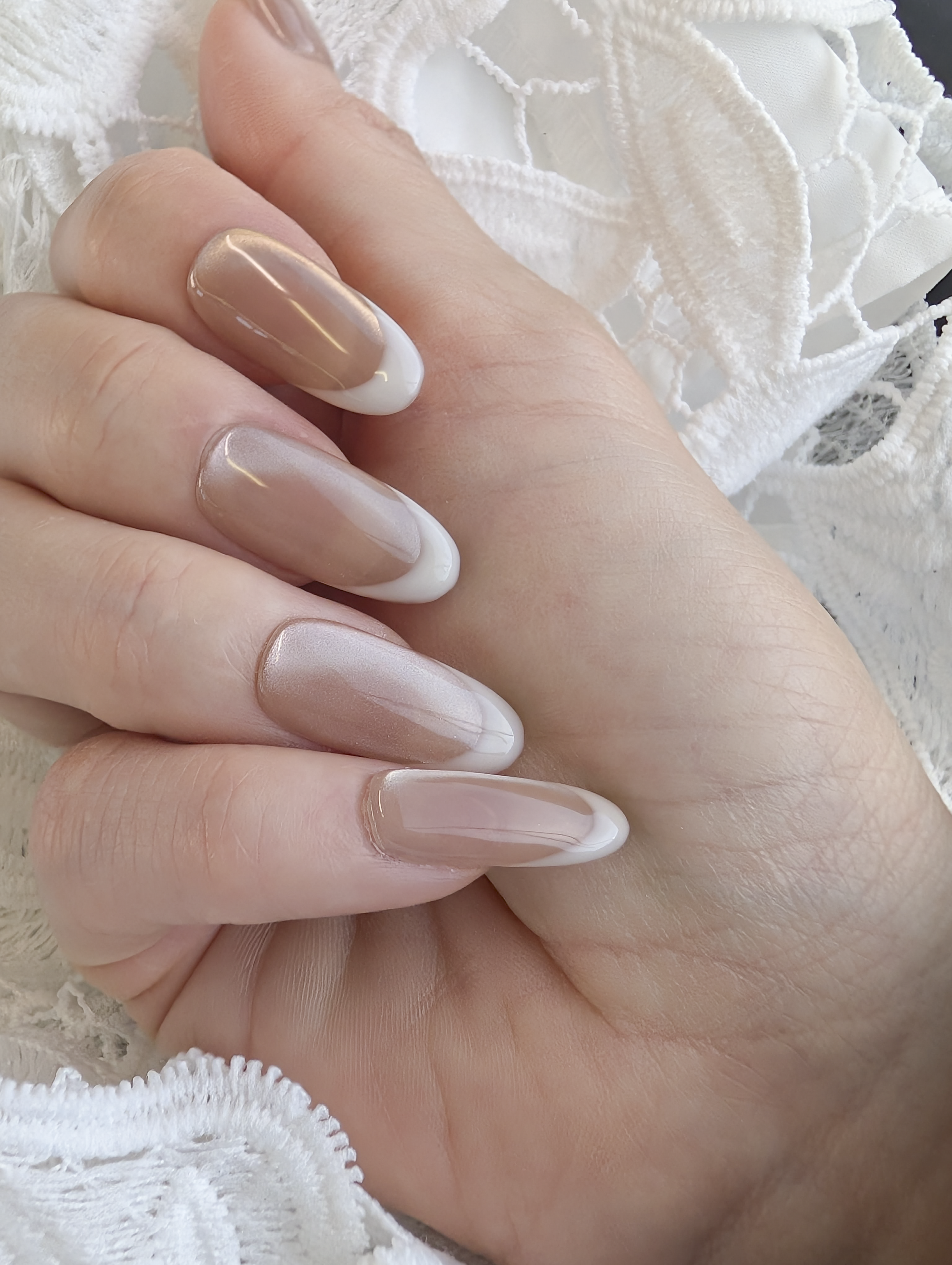 Hand with nude-colored nail polish on a white lace background