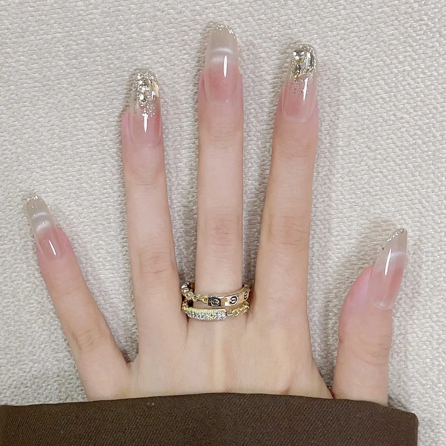 Hand with long, decorated nails and a gold ring on a textured background