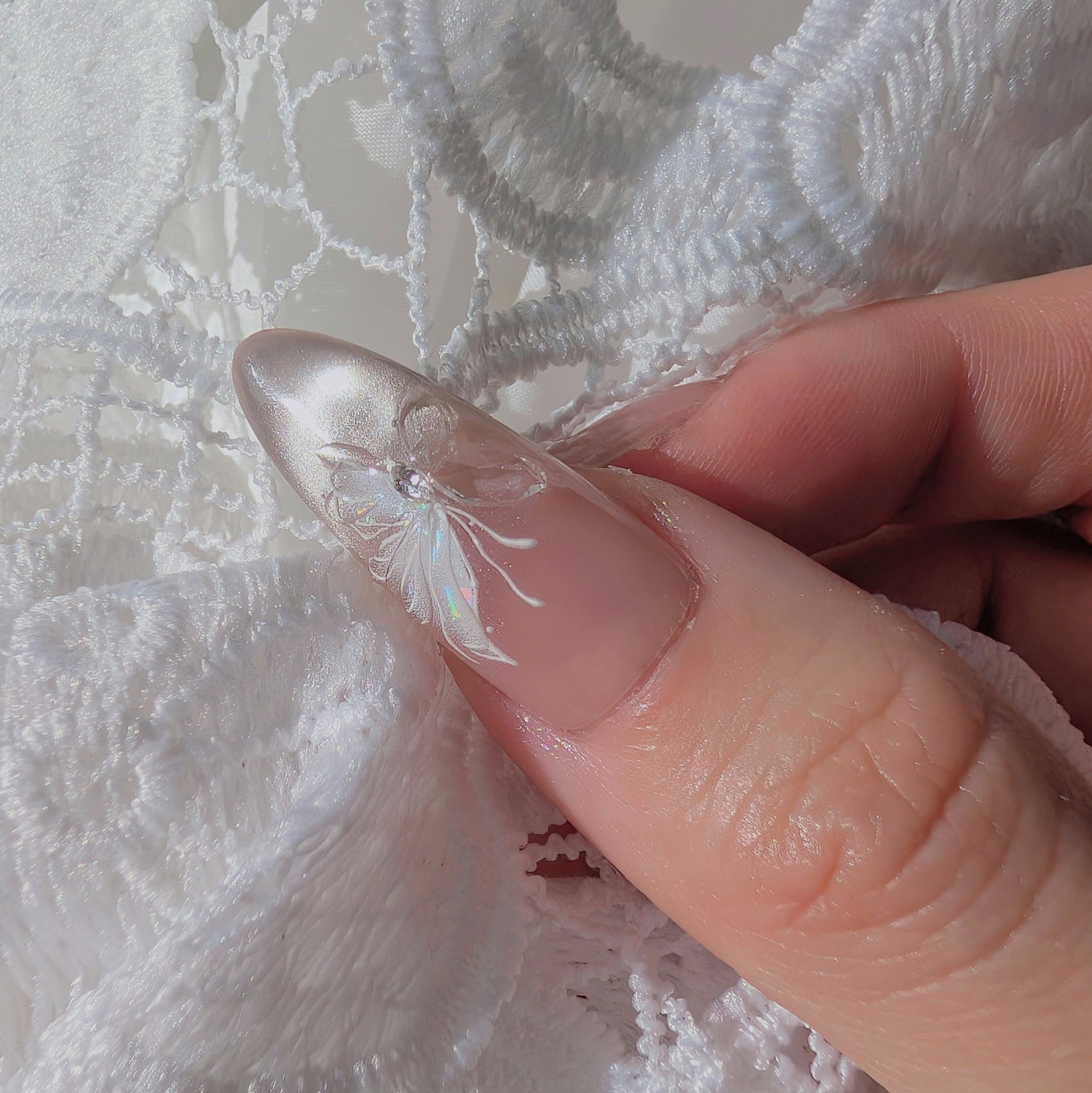 Close-up of a hand holding a small decorative item against white lace fabric