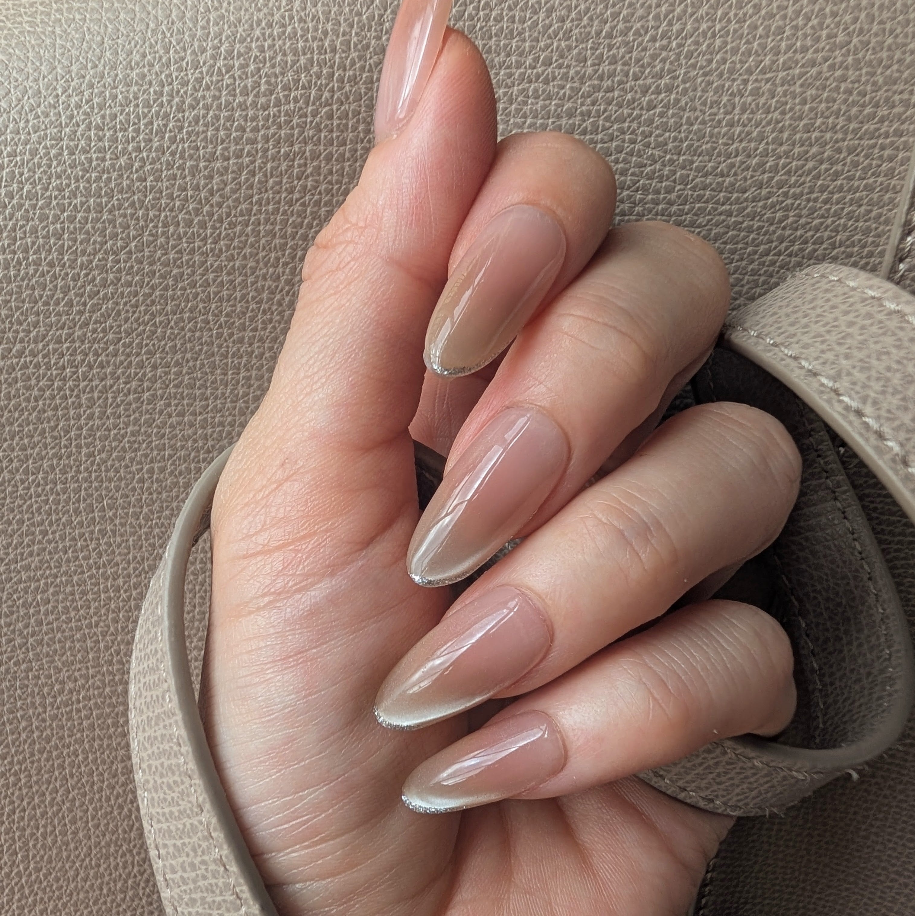 Hand with almond-shaped nails and a neutral color scheme against a beige background