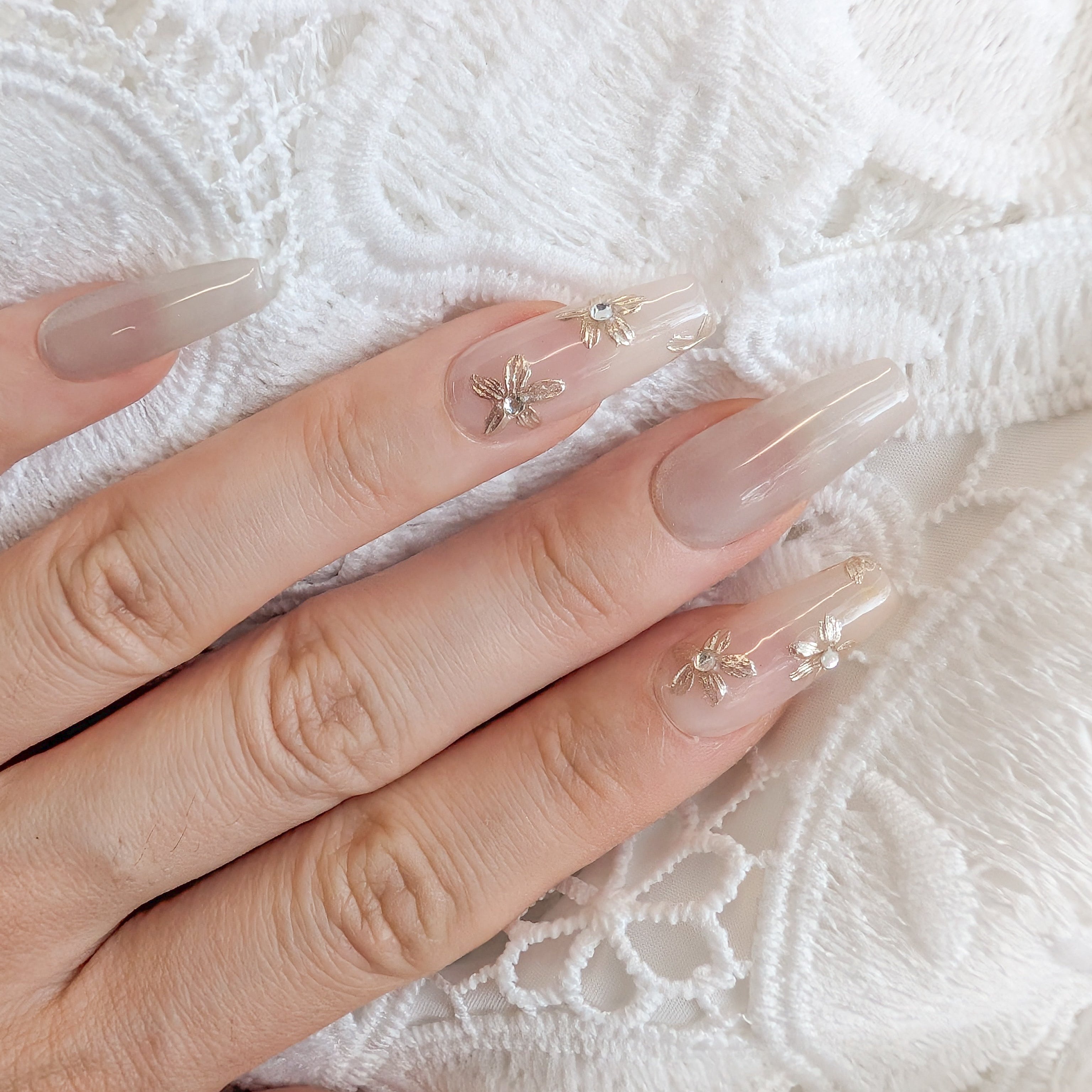 Hand with long, clear nails featuring small decorative elements on a white lace background.