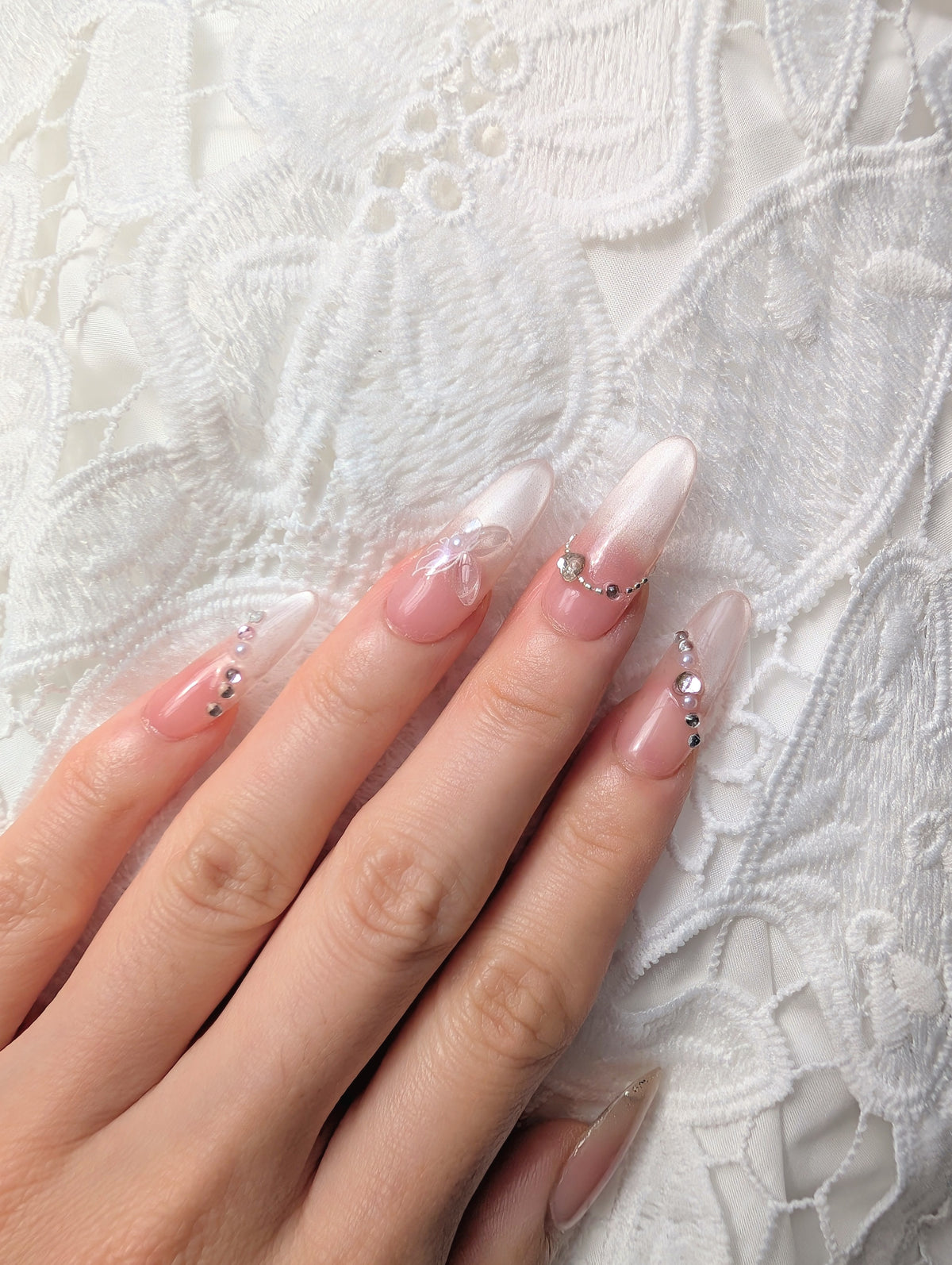 Hand with pink nail polish and decorative elements on a white lace background